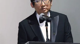 Professional man in glasses and formal attire speaking at podium with microphone during presentation