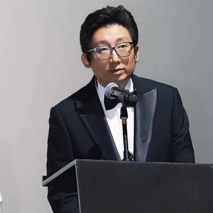 Professional man in glasses and formal attire speaking at podium with microphone during presentation