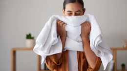 Woman wrapping white towel around herself in spa setting wearing brown robe