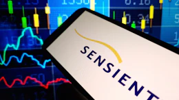 Sensient logo displayed on smartphone screen with financial trading charts and market data in background