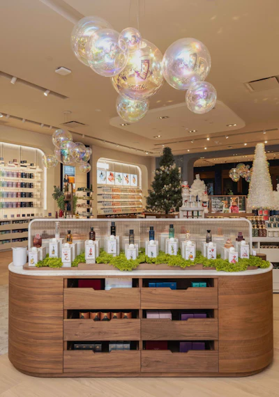 Modern beauty retail store interior with curved wooden counter displaying skincare products, iridescent hanging spheres, and holiday decorations