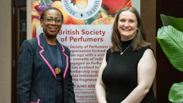 Two women smiling at British Society of Perfumers event with floral banner backdrop