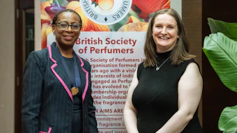 Two women smiling at British Society of Perfumers event with floral banner backdrop