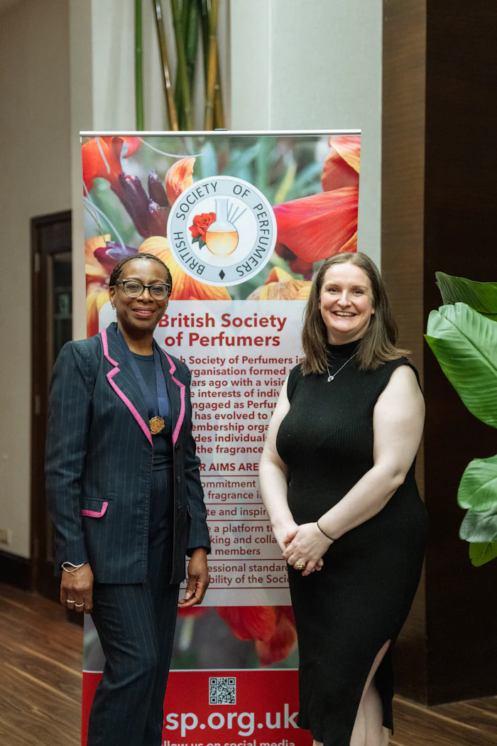 Two women smiling at British Society of Perfumers event with floral banner backdrop