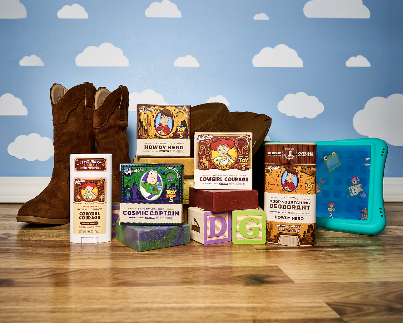 Toy Story branded product collection including cowboy boots, deodorant, soap, and accessories arranged on wooden surface with cloud backdrop