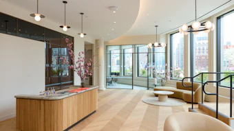 Modern luxury apartment lobby with wooden reception desk, contemporary seating, floor-to-ceiling windows overlooking city skyline