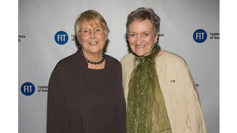 Two women smiling at Fashion Institute of Technology event with FIT logos on backdrop