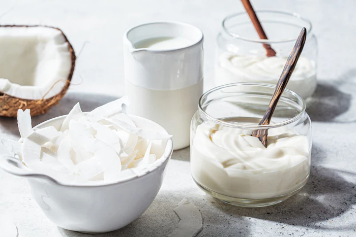 Coconut milk, shredded coconut, and creamy yogurt arranged with wooden spoons on a light surface