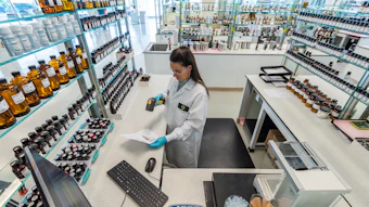 Scientist in lab coat working at bench with shelves of bottles and products in modern laboratory