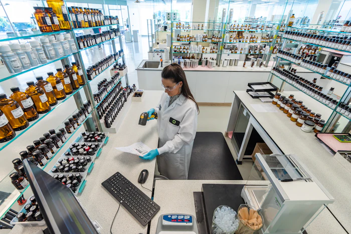 Scientist in lab coat working at bench with shelves of bottles and products in modern laboratory