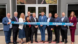 Group of business professionals holding blue Kerry ribbon at ribbon-cutting ceremony outside building