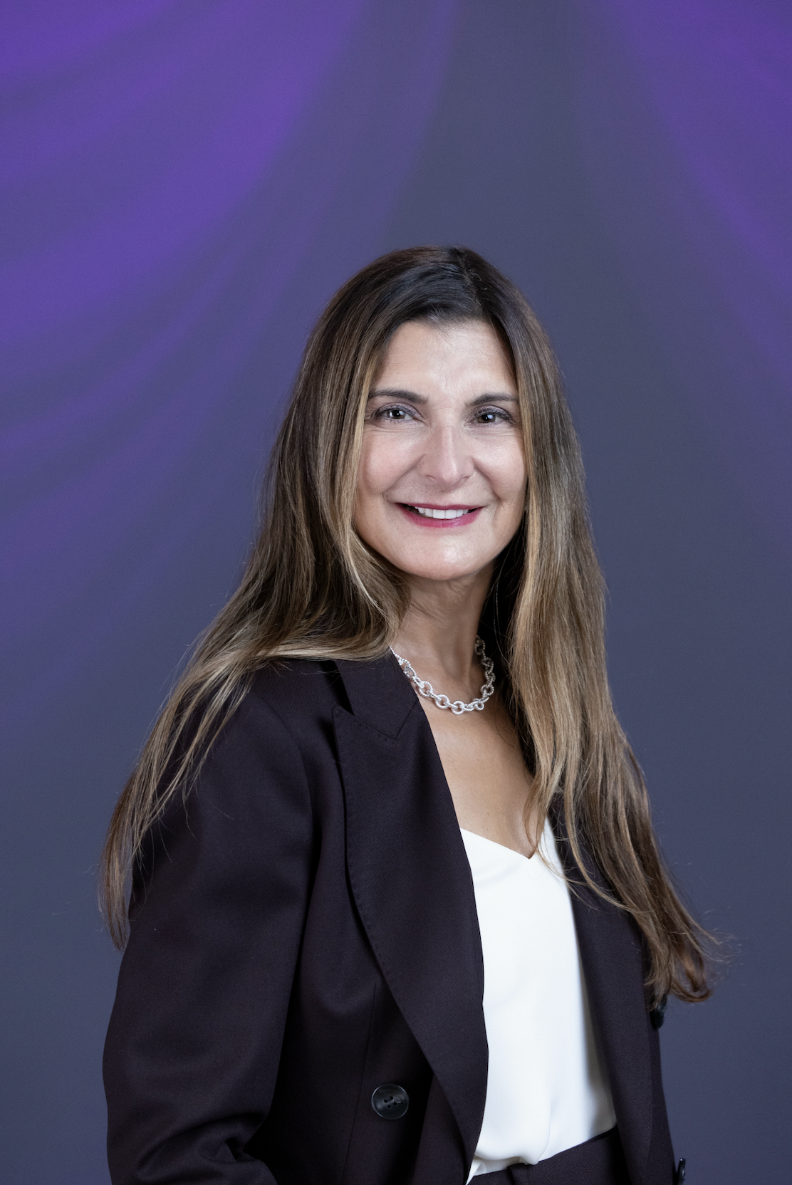 Professional headshot of a woman in black blazer and white blouse against purple background
