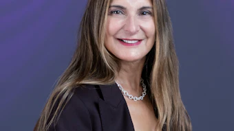 Professional headshot of a woman in black blazer and white blouse against purple background
