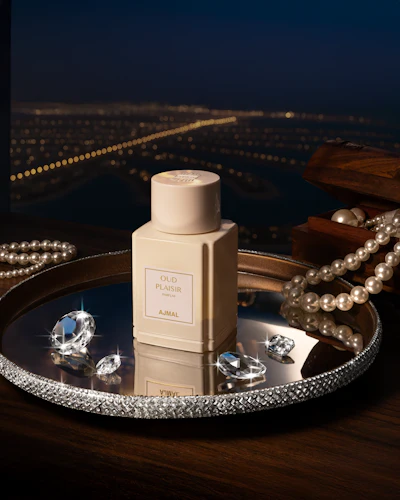 Ajmal Oud Plaisir luxury perfume bottle displayed on crystal-adorned tray with pearls and diamonds against city lights backdrop