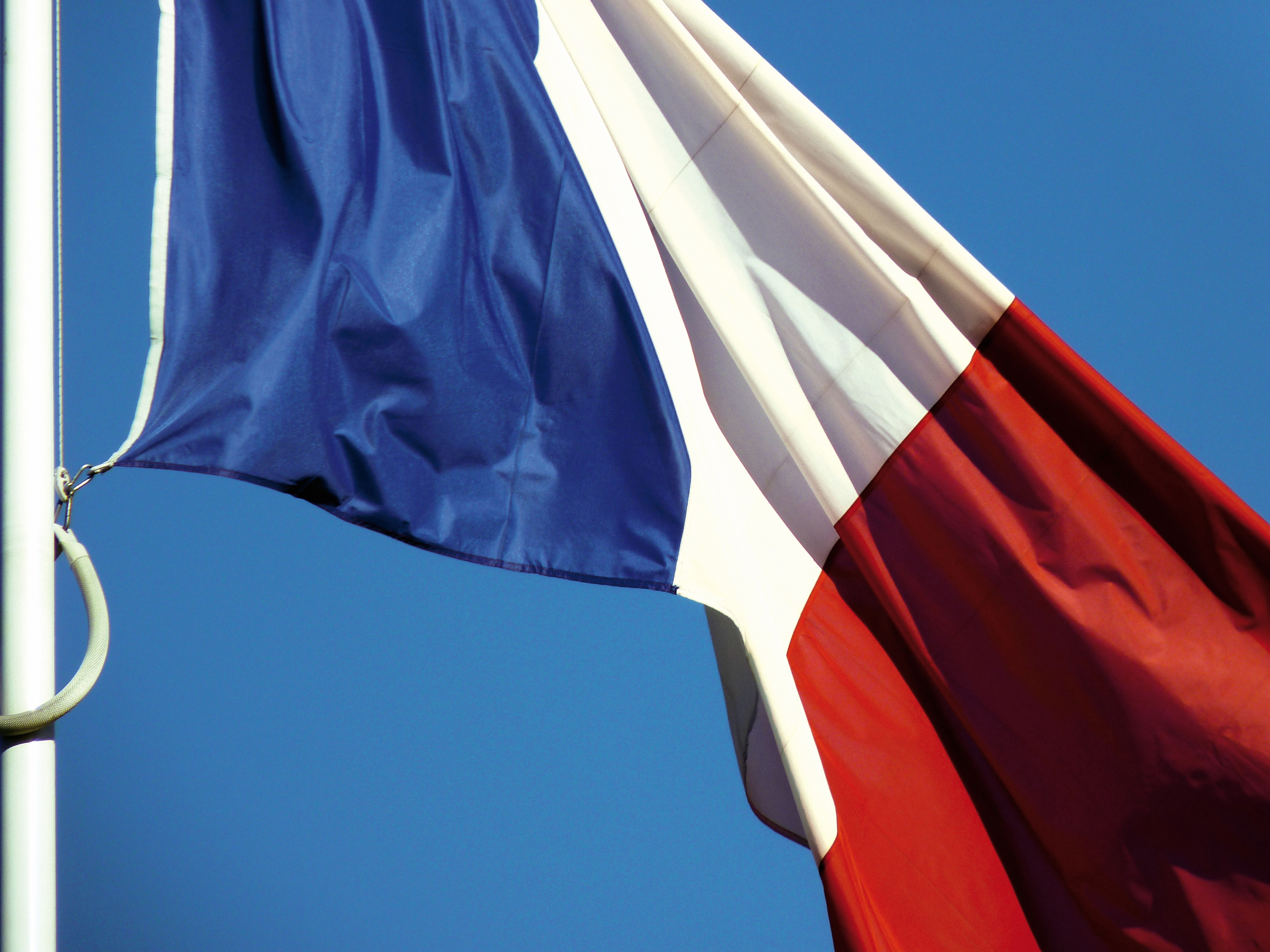 French flag with blue, white, and red vertical stripes flying on a flagpole against a clear blue sky