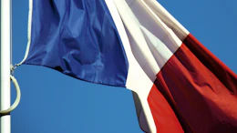 French flag with blue, white, and red vertical stripes flying on a flagpole against a clear blue sky