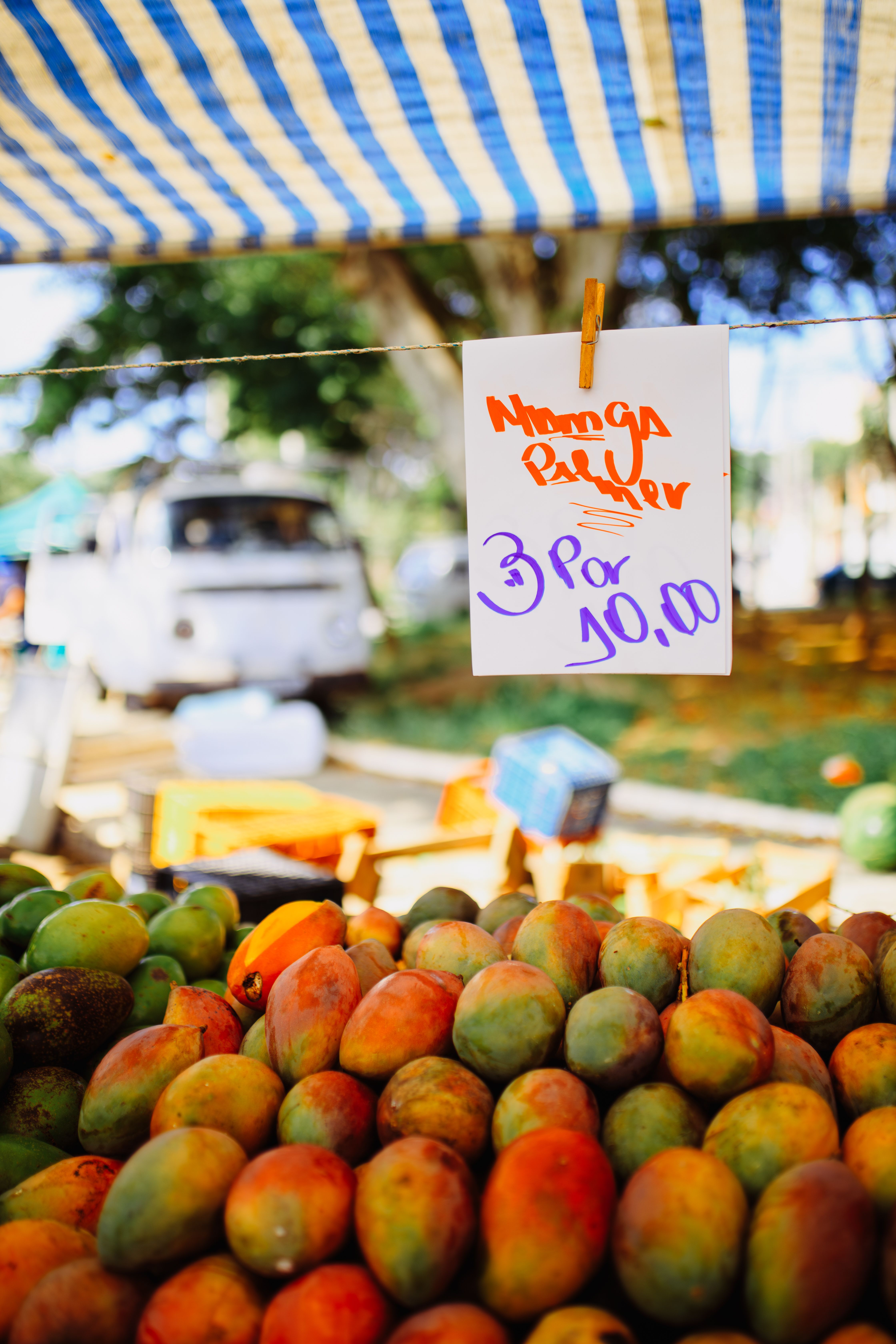 Handwritten price sign for mango pulp at a farmer's market stand with fresh mangoes displayed below