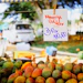 Handwritten price sign for mango pulp at a farmer's market stand with fresh mangoes displayed below