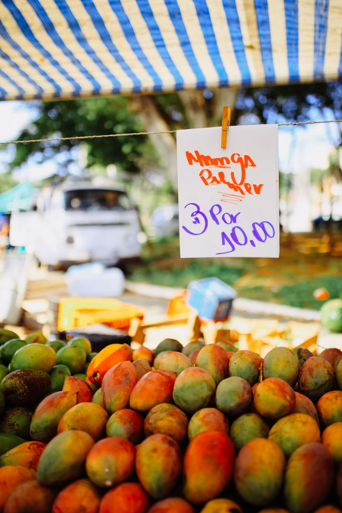 Handwritten price sign for mango pulp at a farmer's market stand with fresh mangoes displayed below