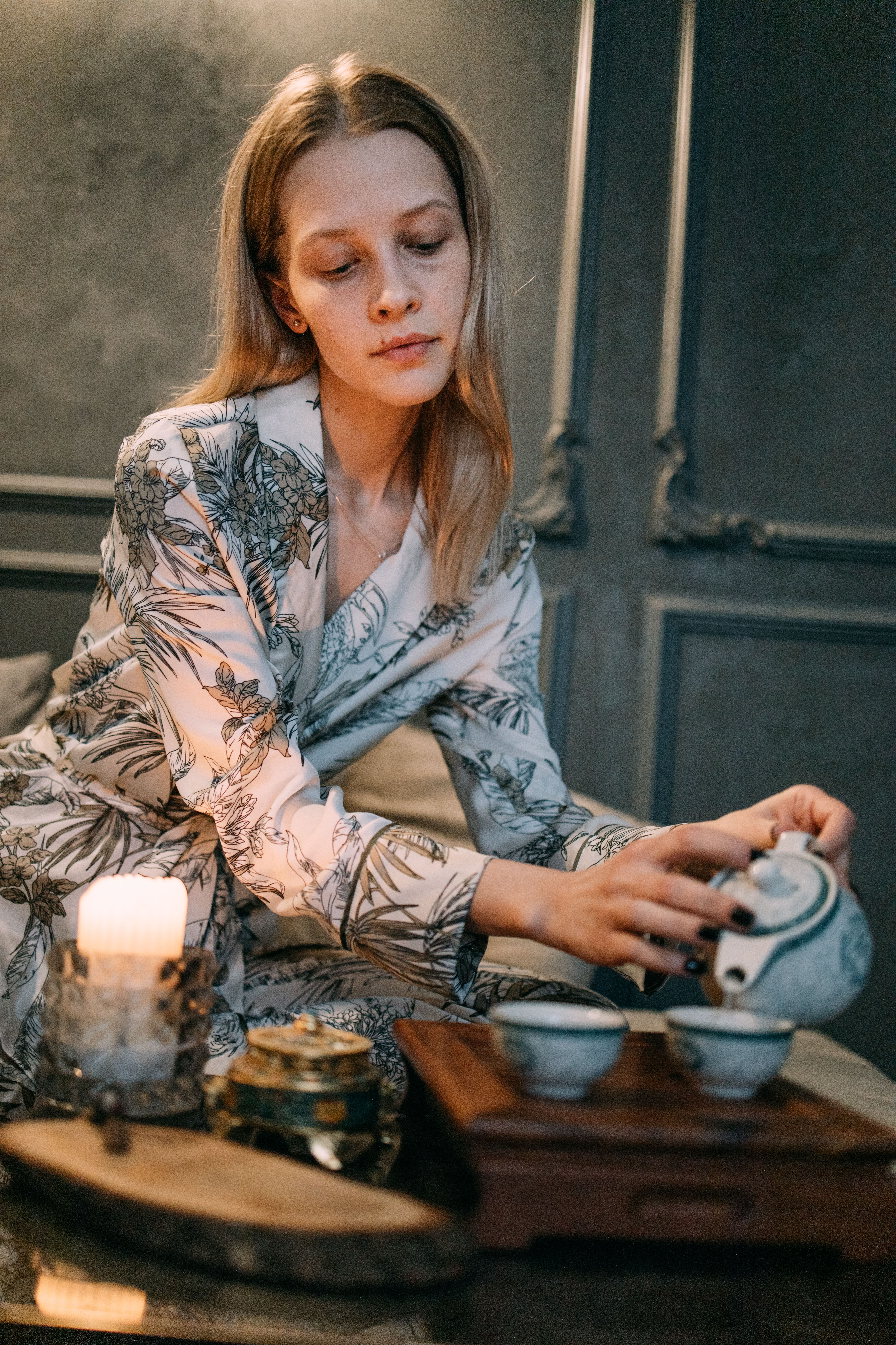 Woman in floral robe performing traditional tea ceremony with ceramic cups and candle
