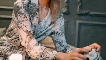 Woman in floral robe performing traditional tea ceremony with ceramic cups and candle