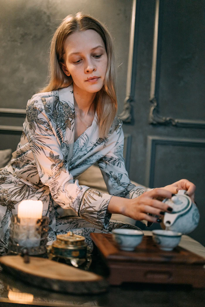 Woman in floral robe performing traditional tea ceremony with ceramic cups and candle