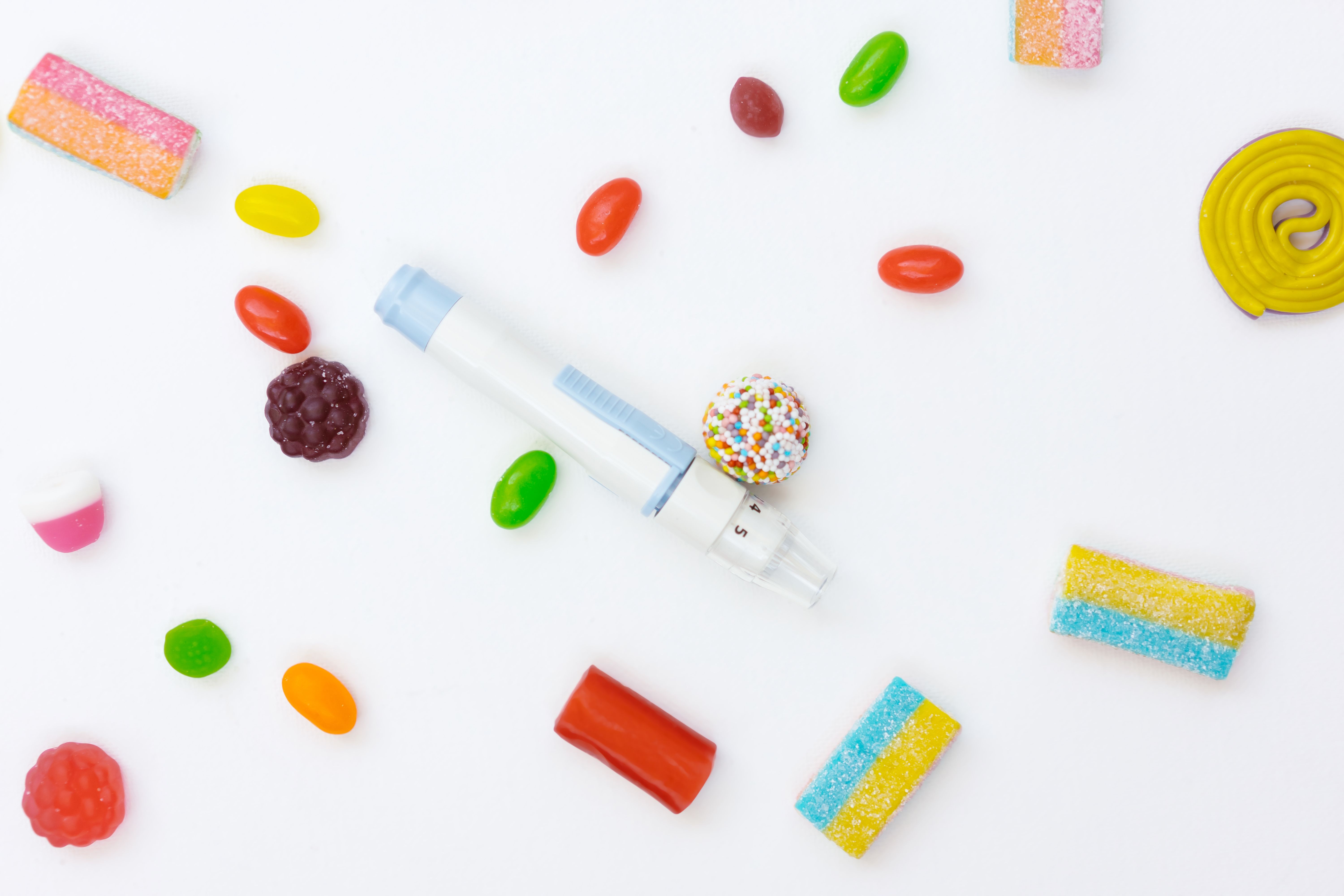 Colorful candies and sweets arranged on white background with candy dispenser in center