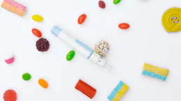 Colorful candies and sweets arranged on white background with candy dispenser in center