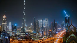 Dubai skyline at night featuring Burj Khalifa and illuminated skyscrapers with busy highway traffic below