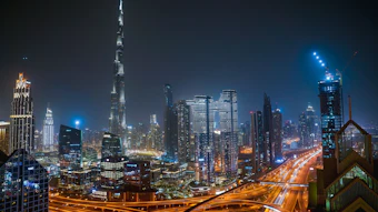 Dubai skyline at night featuring Burj Khalifa and illuminated skyscrapers with busy highway traffic below