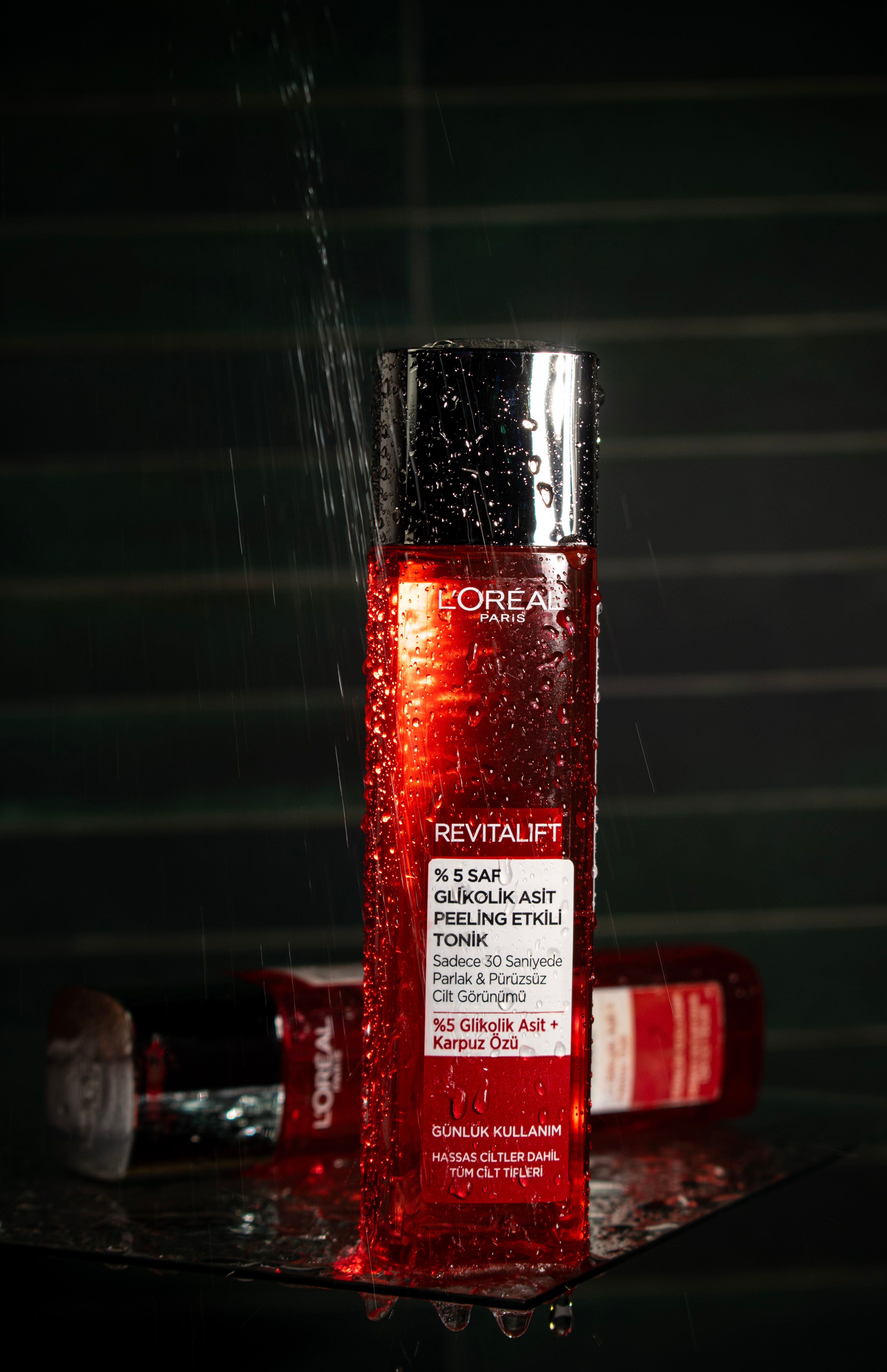 L'Oréal Revitalift glycolic acid peeling tonic bottle with water droplets under dramatic lighting