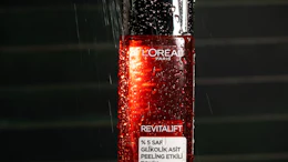L'Oréal Revitalift glycolic acid peeling tonic bottle with water droplets under dramatic lighting