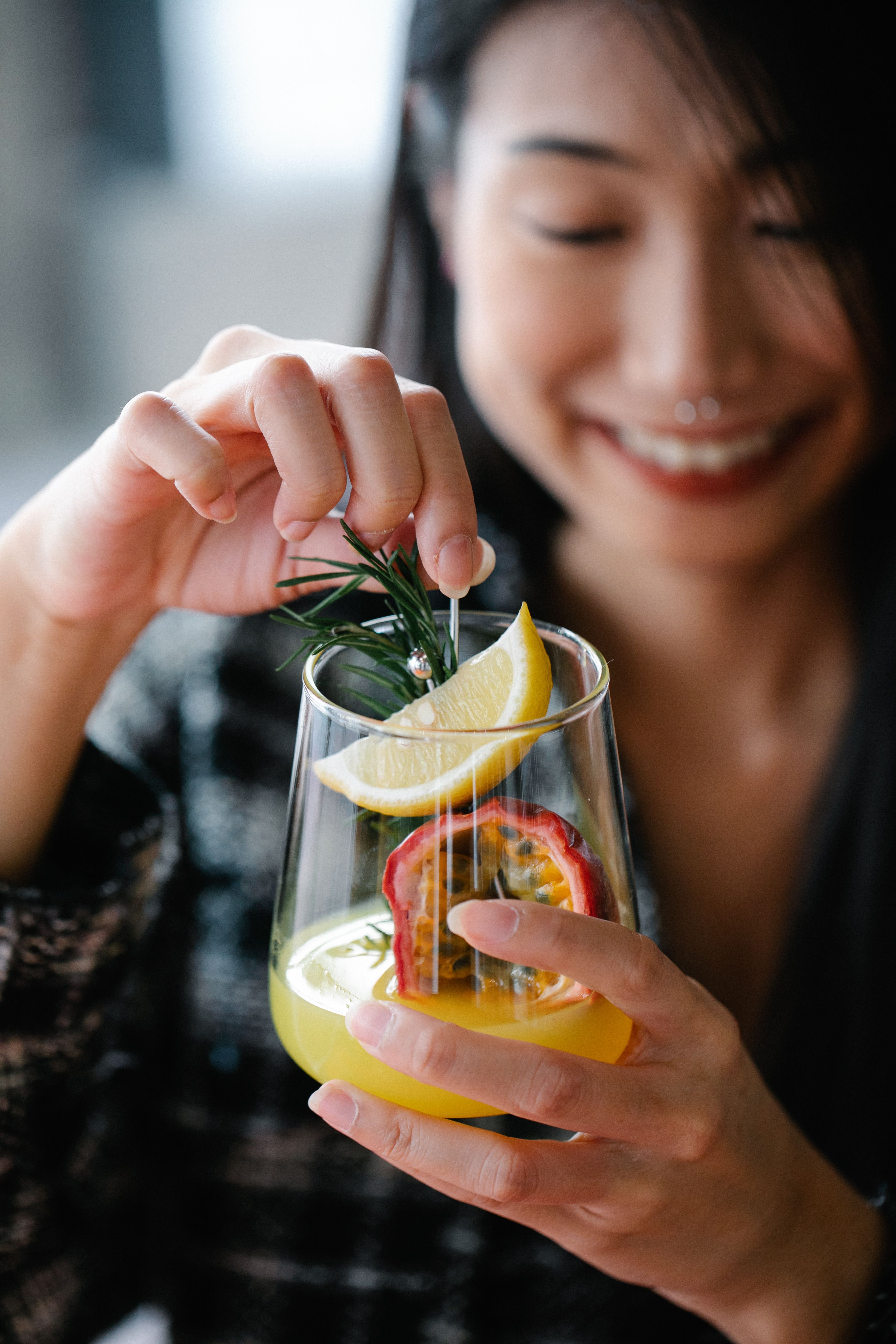 Woman smiling while holding a citrus cocktail garnished with lemon, rosemary, and passion fruit