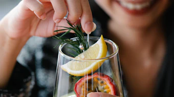 Woman smiling while holding a citrus cocktail garnished with lemon, rosemary, and passion fruit
