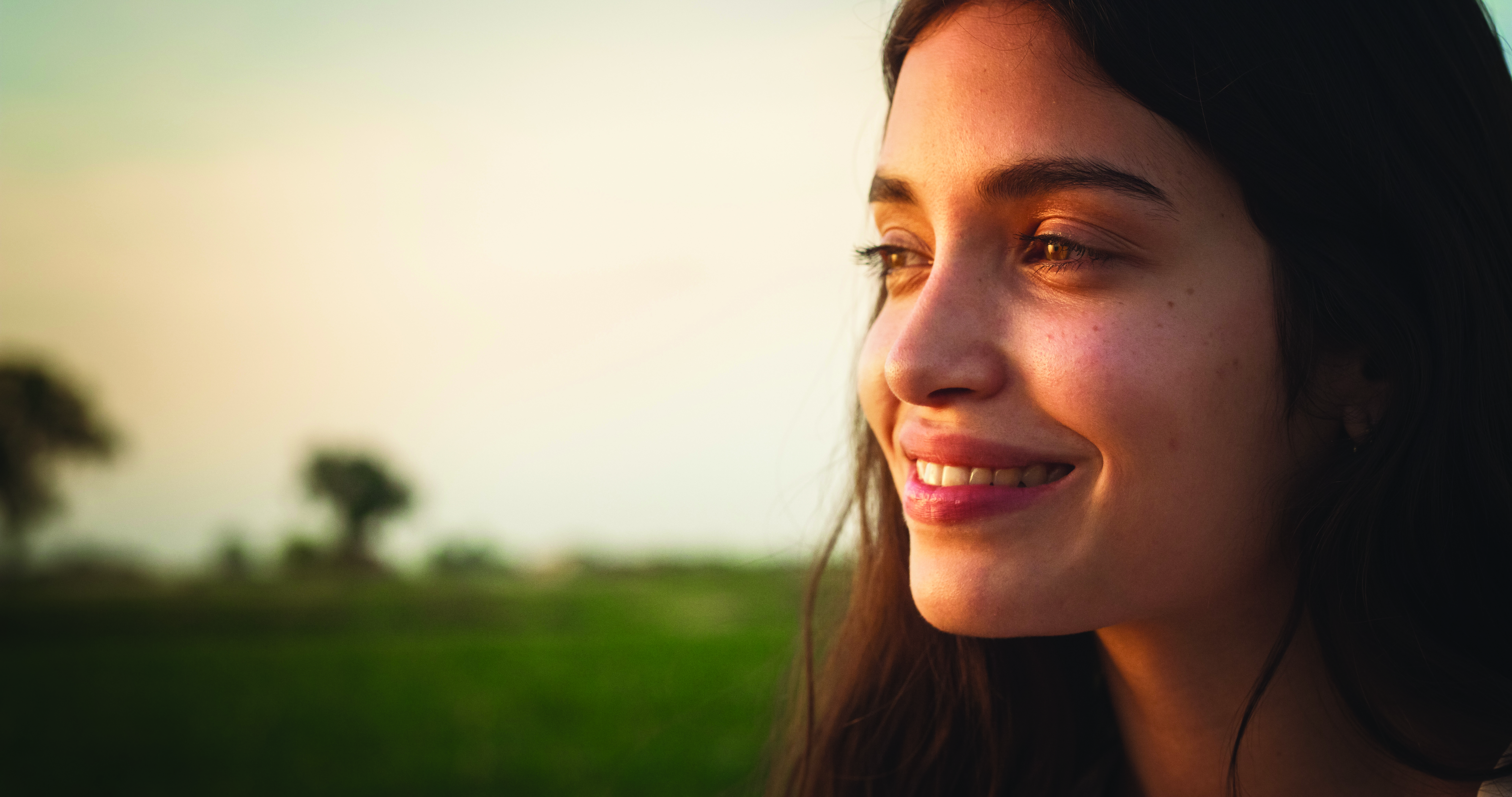 Woman smiling outdoors at sunset with blurred green field in background