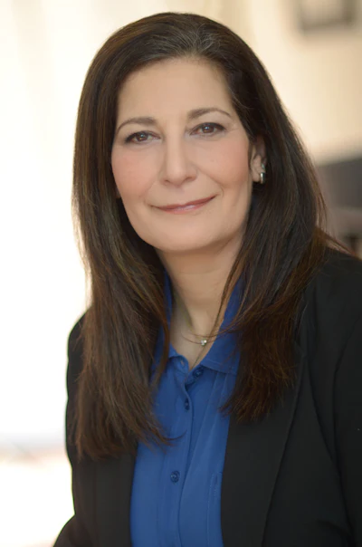 Professional headshot of a woman with long dark hair wearing a blue shirt and black blazer